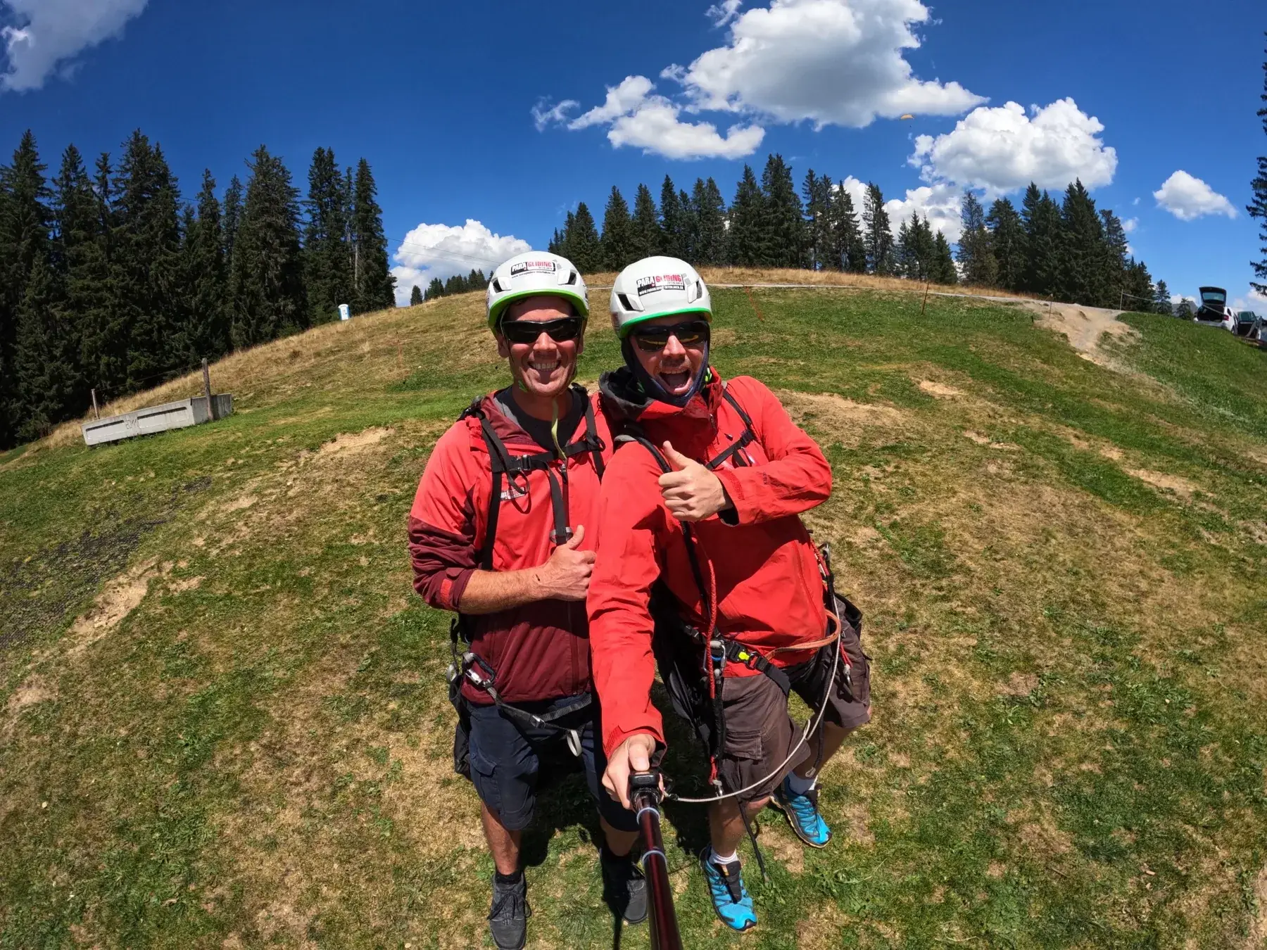 Tandem pilot and passenger in harnesses and helmets at a grassy launch above Interlaken